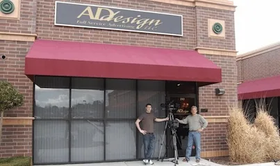 Brick storefront with maroon awning and large windows, three people standing in front of entrance