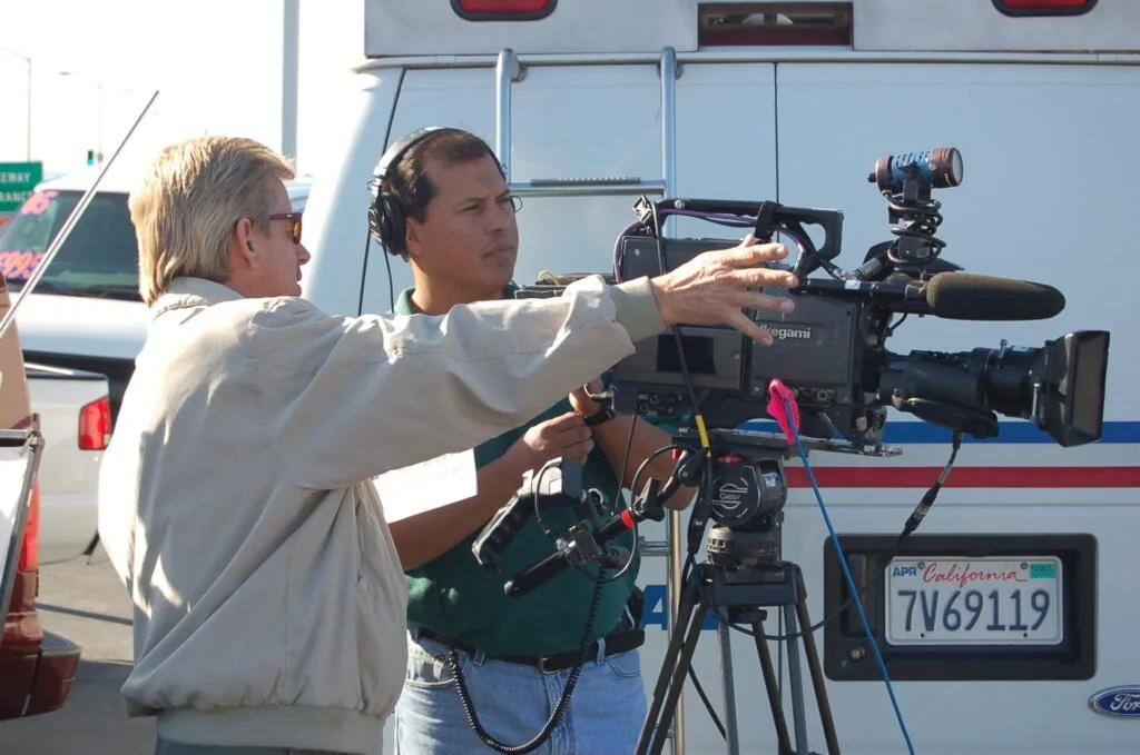 Two men operating professional video camera equipment in front of broadcast van
