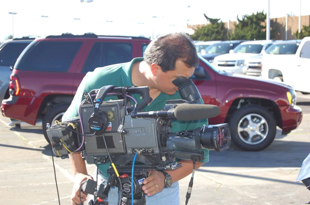 Cameraman holding professional video camera in parking lot with cars in background