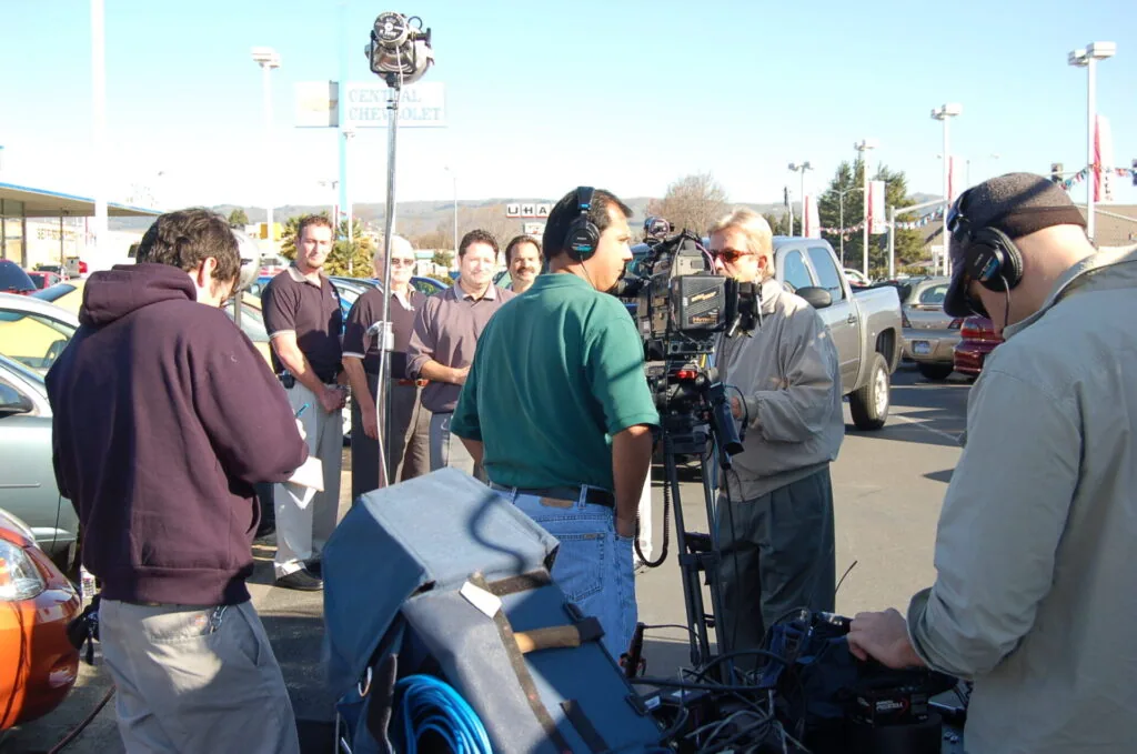 Film crew and production team operating camera equipment in a parking lot during daytime shooting